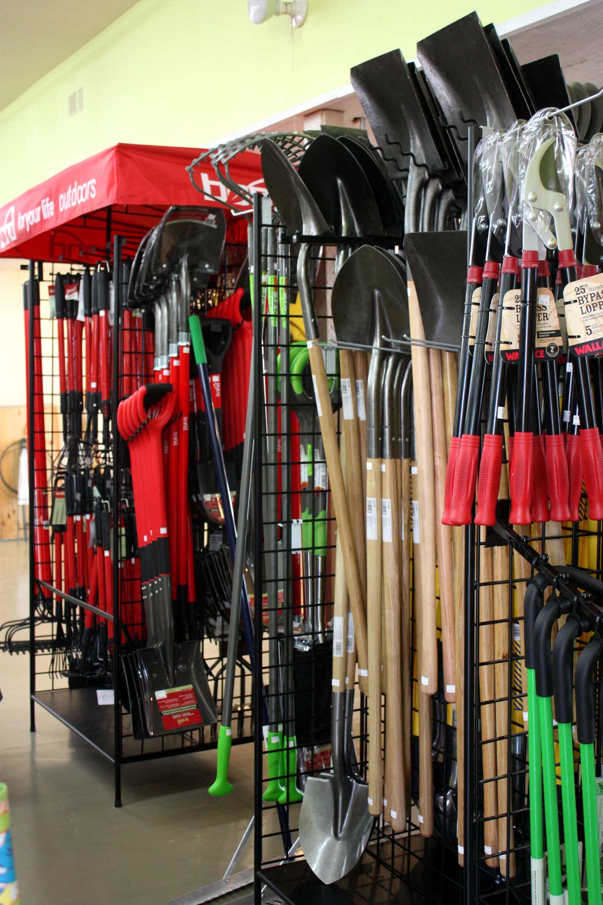 A wall full of hanging shovels and other tools, all part of the large selection of garden supplies at Bark & Garden Center.